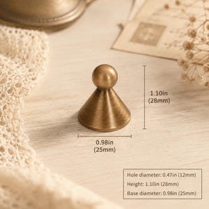 May include: A brass-toned metal knob with a conical base and a spherical top. The knob has a height of 1.10 inches, a base diameter of 0.98 inches, and a hole diameter of 0.47 inches, as indicated by the technical specifications in the image.