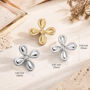 Pode incluir: Três puxadores de metal para armários em forma de flor de quatro pétalas, um dourado e dois prateados. Cada puxador mede 52 mm de altura e 22 mm de largura. O design apresenta pétalas lisas em forma de gota que irradiam de um quadrado central.