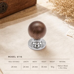 Pode incluir: Um puxador esférico de madeira de nogueira castanho-escura com uma base de liga de zinco prateada polida. O produto está rotulado como Modelo 6116 com distância entre furos de 24 mm, 24 mm de comprimento, 24 mm de largura, 35 mm de altura e 18 g.