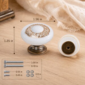 May include: A white ceramic cabinet knob with a gold-colored floral pattern and a bronze-toned base. The knob measures 1.56 inches in diameter and 1.25 inches in height. Included are four screws measuring 1.00, 0.78, 0.55, and 0.43 inches, plus washers.