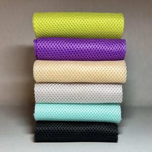 Puede incluir: Una pila vertical de seis toallas refrescantes rectangulares con tejido de malla texturizado. Las toallas están dispuestas en una secuencia de colores de arriba a abajo: verde lima, morado, beige, blanco, turquesa claro y negro, con un patrón de rejilla.