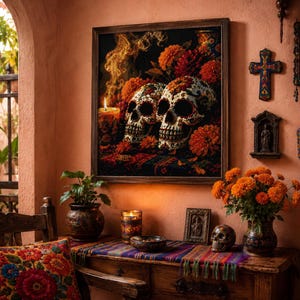May include: A framed wall art piece depicting two decorated sugar skulls surrounded by orange marigold flowers and a lit candle with rising smoke. The artwork is displayed on a peach-colored wall above a wooden table with a colorful woven runner.