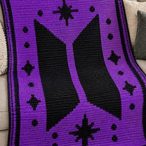 Könnte beinhalten: Eine rechteckige Häkeldecke mit einem leuchtend violetten Hintergrund und einem großen, mittig platzierten schwarzen geometrischen Logo. Das Design wird durch kleine schwarze Stern- und Punktmotive ergänzt, die symmetrisch um das zentrale Emblem angeordnet sind.