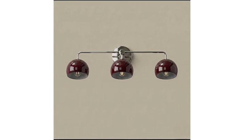 May include: A wall-mounted light fitting featuring three glossy, deep burgundy, dome-shaped shades attached to a polished chrome horizontal bar. The fitting includes a circular chrome wall plate at the centre, supporting the three individual light heads.