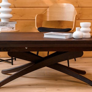Puede incluir: Una mesa de centro de madera de color marrón oscuro con una superficie rectangular y una base de patas cruzadas en forma de tijera. La mesa presenta una superficie lisa y plana, con una construcción robusta y un acabado de veta de madera.