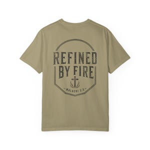 May include: A khaki-colored short-sleeve t-shirt featuring a dark graphic on the back. The design includes a circular border enclosing the text REFINED BY FIRE, a cross symbol, and the scripture reference Malachi 3:3 in a distressed font.