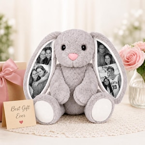 Könnte beinhalten: Ein grauer Plüschhase mit langen Ohren, die mit schwarz-weißen Fotos bedruckt sind. Der Hase hat eine rosa Nase und weiße Flecken an den Pfoten. Links daneben steht eine kleine Karte mit dem Text Best Gift Ever und einem roten Herzsymbol.