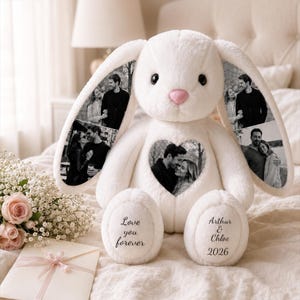 Puede incluir: Un conejo de peluche color crema con impresiones fotográficas en blanco y negro en sus largas orejas y un parche en forma de corazón en el pecho. Los pies tienen bordado el texto Love you forever y Arthur & Chloe 2026 en negro.