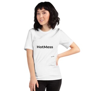 以下が含まれることがあります： 胸の中央に太い黒文字でHotMessとプリントされた白い半袖Tシャツ。このTシャツはクルーネックで標準的なフィット感があり、メインのグラフィックの下には小さな二次的なテキスト要素が配置されています。