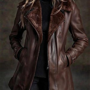 May include: A brown leather jacket featuring a dark brown faux fur collar and lapels, a full-length front zipper, and adjustable buckle straps on the cuffs. The jacket is worn over a black ribbed turtleneck sweater and black pants.