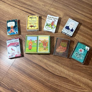 May include: Eight decks of playing cards featuring various designs, including a St. Louis Cardinals deck, a Lures of the Past deck, a Golf Playing Cards deck, a Johann Sebastian Bach deck, a double deck set with golf scenes, a New Hampshire deck, and an Olympia Giant Face deck.