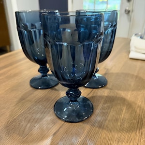 May include: Three matching dark blue glass goblets with a vertical ribbed pattern on the bowl, a short stem with a decorative knob, and a circular base. The glassware features a translucent deep blue color and a classic footed design.