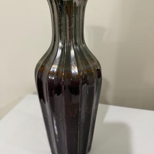 May include: A tall, fluted ceramic vase with a glossy finish. The body features a deep, dark burgundy color at the base that transitions into a metallic, gunmetal gray glaze toward the narrow neck and flared rim, creating a gradient effect.