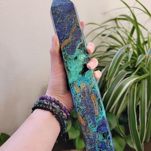 May include: A tall, polished azurite and malachite crystal tower featuring a vibrant mix of deep blue, bright green, and earthy brown mineral veins. The stone has a faceted, pointed top and a textured, natural surface with visible crystalline cavities.