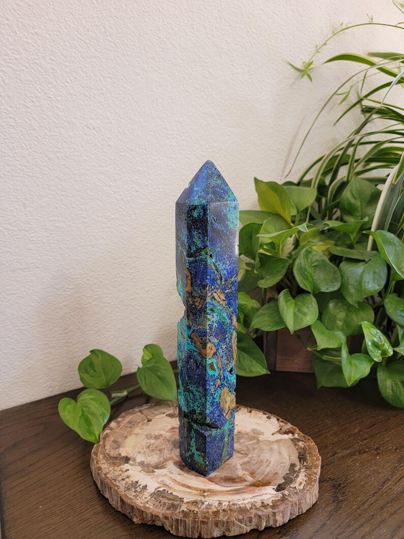 May include: A tall, faceted crystal tower featuring a vibrant mix of deep royal blue, turquoise, and earthy brown mineral inclusions. The stone has a polished, pointed top and a natural, rugged texture along its vertical sides, standing upright.