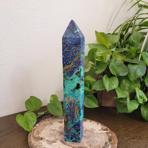 May include: A tall, six-sided crystal tower featuring a vibrant mix of deep royal blue, bright turquoise, and earthy brown mineral veins. The polished stone has a pointed top and a textured, natural surface with small cavities throughout the structure.
