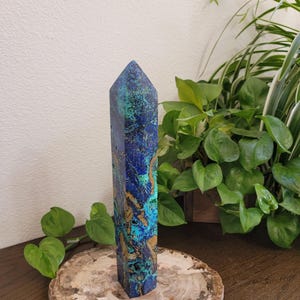 May include: A tall, faceted crystal tower featuring a vibrant, marbled pattern of deep royal blue, bright turquoise, and earthy tan mineral inclusions. The stone has a polished, smooth surface with a pointed, pyramidal top and a hexagonal base.