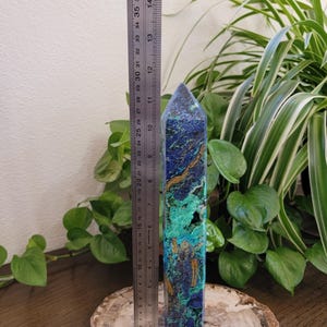 May include: A tall, faceted crystal tower featuring a vibrant mix of deep blue, bright turquoise, and golden-brown mineral veins. A metal ruler placed alongside the crystal indicates a height of approximately 11.5 inches for the stone point.