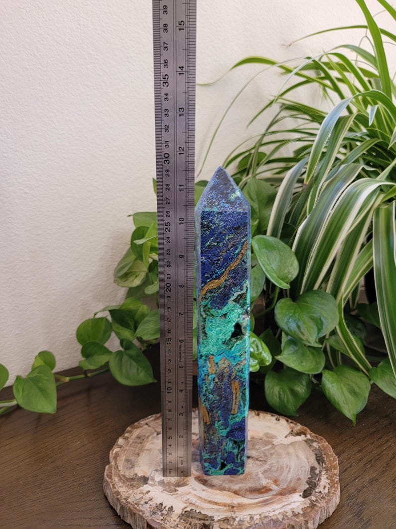 May include: A tall, faceted crystal tower featuring a vibrant mix of deep blue, bright turquoise, and golden-brown mineral veins. A metal ruler placed alongside the crystal indicates a height of approximately 11.5 inches for the stone point.