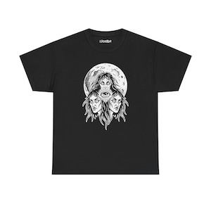 Pode incluir: Camiseta preta com uma ilustração em preto e branco de três rostos, um olho e uma lua cheia. O texto "Naked Bar" está impresso no topo. O design é detalhado e intrincado.