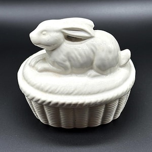 May include: White ceramic bunny rabbit figurine sitting inside a white ceramic basket with a woven design.
