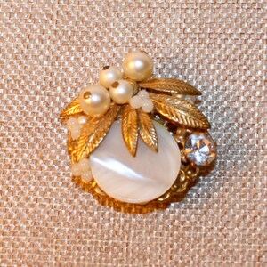 May include: A gold-tone brooch with a white mother-of-pearl center and a cluster of faux pearls and rhinestones.