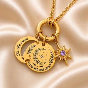 Peut inclure: Un collier doré avec un pendentif circulaire gravé d'un croissant de lune, d'étoiles et du texte "STAY WILD MOON CHILD". Un charm en forme de croissant avec l'inscription "To the moon" et une étoile avec une pierre violette sont fixés.