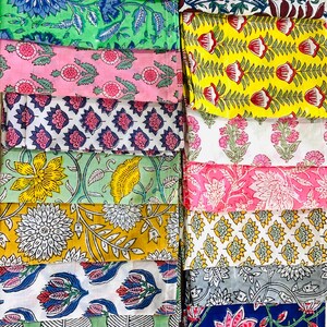 May include: A collection of folded fabric squares featuring diverse block-printed floral and botanical patterns. The textiles display a vibrant array of colours including yellow, pink, green, blue, and white, with intricate petal and leaf motifs.