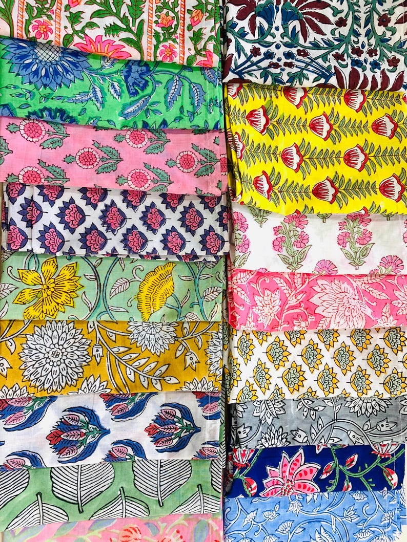 May include: A collection of folded fabric squares featuring diverse block-printed floral and botanical patterns. The textiles display a vibrant array of colours including yellow, pink, green, blue, and white, with intricate petal and leaf motifs.