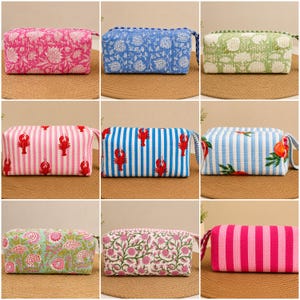 May include: A collection of nine rectangular quilted fabric pouches featuring various patterns including floral prints, vertical stripes, and lobster motifs in colors such as pink, blue, green, and white, each with a side carry handle.