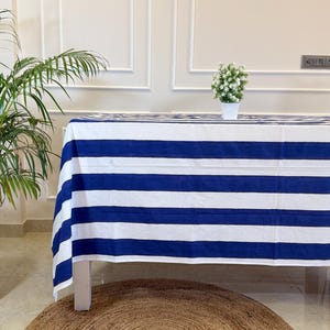 Può includere: Una tovaglia rettangolare caratterizzata da un motivo a larghe strisce orizzontali blu navy e bianche. Il tessuto copre un tavolo, mostrando un design a righe coerente su tutta la superficie, offrendo un aspetto pulito e uniforme.