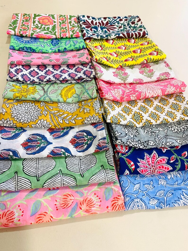 May include: A collection of folded cotton fabric squares featuring various block-printed floral and botanical patterns in vibrant colours including yellow, pink, blue, green, and grey. Each piece displays distinct motifs like leaves, petals, and stems.