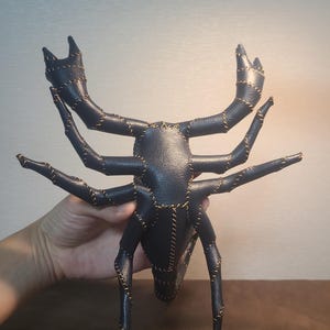 May include: A dark navy blue scorpion-shaped object constructed from textured material with visible light tan stitching along the seams. The creature features two large front pincers, eight segmented legs, and a curved tail section.