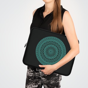 Può includere: Custodia nera per laptop con un design mandala turchese. La custodia ha una chiusura a cerniera ed è progettata per proteggere un laptop. Il mandala è un motivo simmetrico e dettagliato. La custodia è tenuta da una persona.