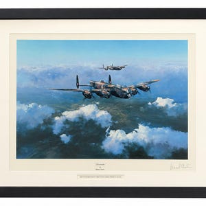 May include: A framed aviation art print titled Lancaster by Robert Taylor, depicting two dark-colored multi-engine propeller aircraft flying over a landscape of white clouds and blue sky, enclosed in a black frame with a cream-colored mat board.