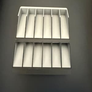 May include: A rectangular storage organizer featuring two stacked rows of six vertical compartments each. The unit is constructed with dark gray outer walls and dividers, contrasted by light gray interior bases for each individual slot.