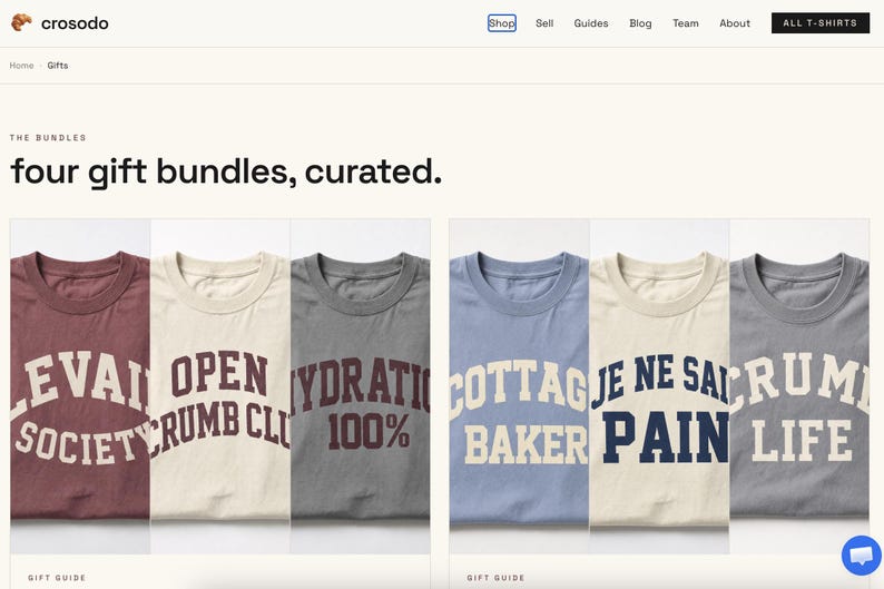 May include: A collection of six t-shirts in various colours including maroon, cream, and grey, each featuring bold, arched lettering with phrases such as LEVAIN SOCIETY, OPEN CRUMB CLUB, HYDRATION 100%, COTTAGE BAKER, JE NE SAIS PAIN, and CRUMB LIFE.