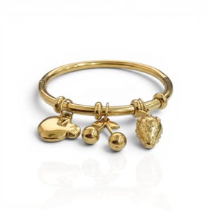 May include: A gold bangle bracelet featuring three charms: a pig, cherries, and a strawberry. The bracelet is made of a shiny, metallic material and is set against a white backdrop. The charms are detailed, adding a playful element to the jewellery.