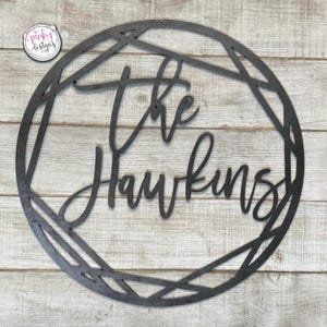 May include: Black metal wreath with a geometric design. The text "The Hawkins" is written in a cursive font.