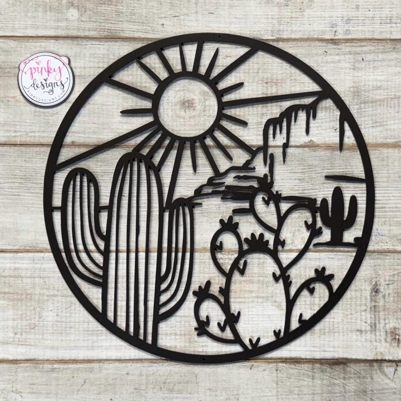 May include: Black metal wall art featuring a desert scene with a sun, mountains, cacti, and prickly pear cactus.