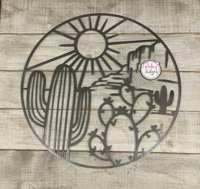 May include: A metal wall art piece depicting a desert scene with a sun, mountains, and cacti. The art is circular and has a black outline.