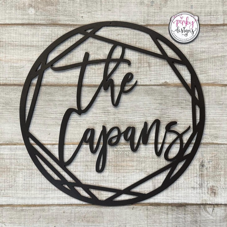 May include: Black wooden sign with a geometric frame and the text "The Capans" in a cursive font.