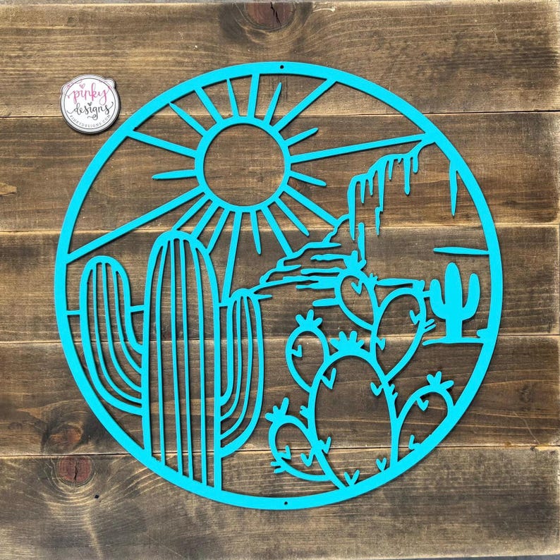 May include: A turquoise blue metal wall art piece depicting a desert scene with cacti, a mountain range, and a sun. The design is circular and has a rustic wood background.