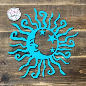 May include: A turquoise blue sun and moon wall decor with a whimsical design. The sun has a face and rays that are stylized with swirls. The moon is a crescent shape with five stars.