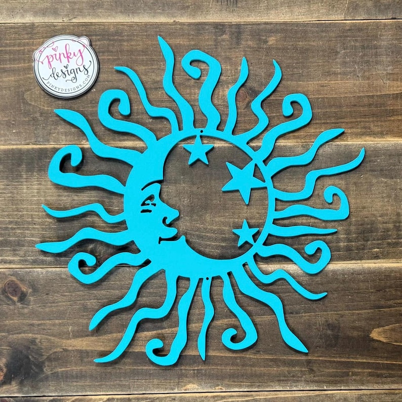 May include: A turquoise blue sun and moon wall decor with a whimsical design. The sun has a face and rays that are stylized with swirls. The moon is a crescent shape with five stars.