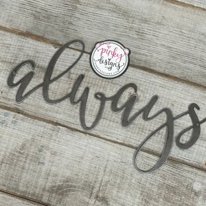 A metal always sign is laid on a light wood background. The metal is left raw metal to show the patina of the natural metal. There is a pinky designs logo located above the metal piece