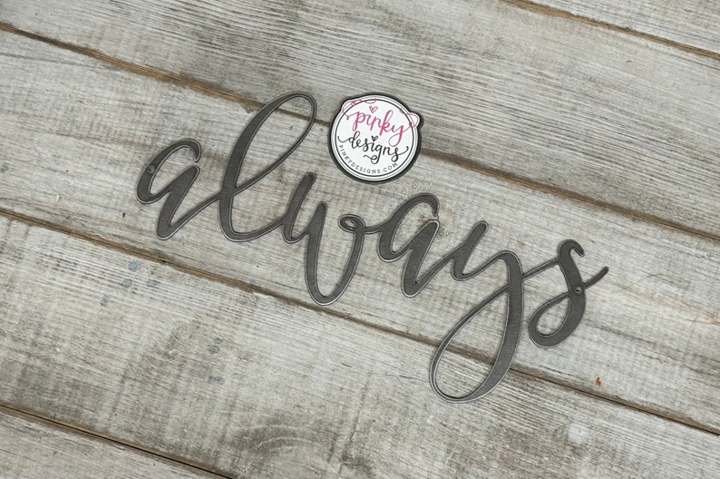 A metal always sign is laid on a light wood background. The metal is left raw metal to show the patina of the natural metal. There is a pinky designs logo located above the metal piece