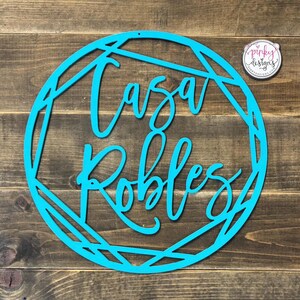 May include: A turquoise blue metal sign with a geometric design. The sign says "Casa Robles" in a cursive font.