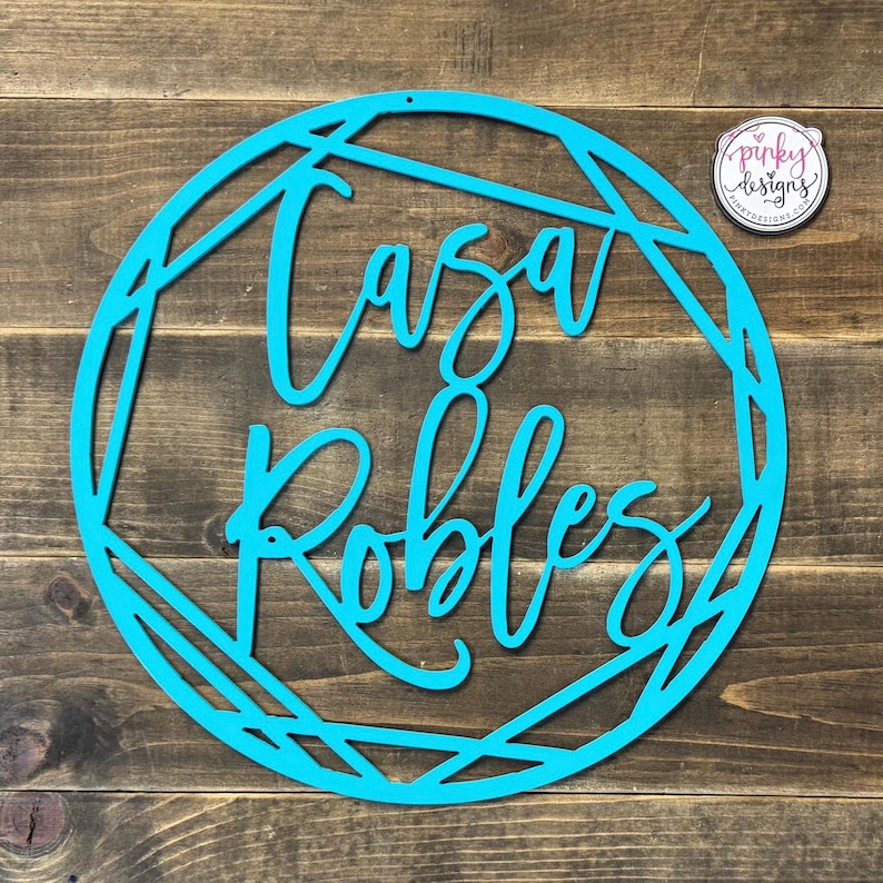 May include: A turquoise blue metal sign with a geometric design. The sign says "Casa Robles" in a cursive font.