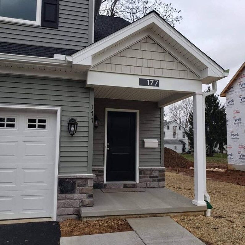 The rectangular address sign is mounted above the Pilars of the exterior of a home. The numbers are painted black and read 177.